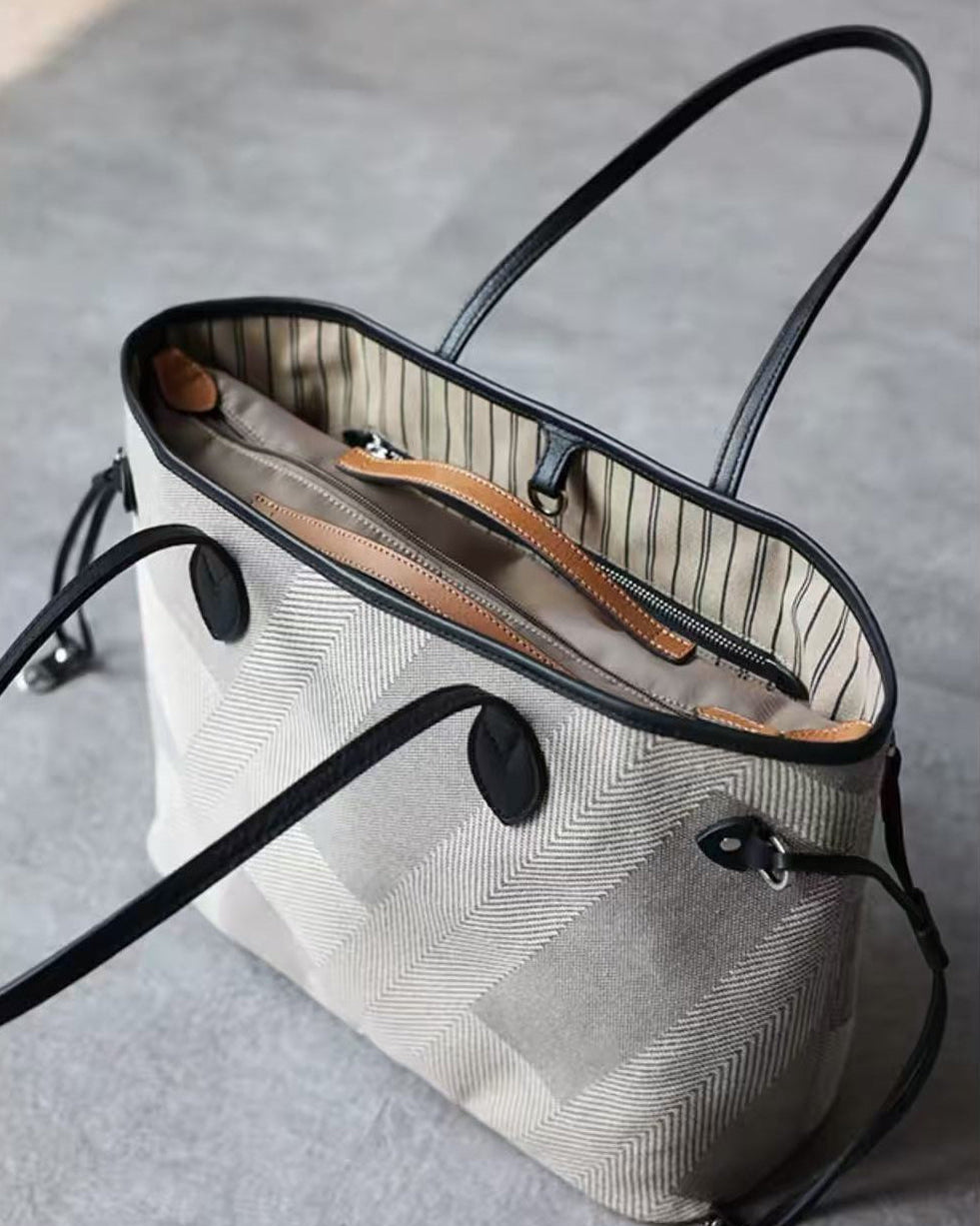 A structured tote bag in a light beige and gray herringbone pattern with black leather trim and handles, shown from an elevated angle on a gray concrete floor.