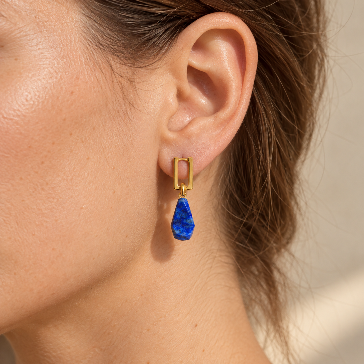 Lapis Accent Stone Earrings worn on one ear, showing the rectangular gold-tone hoop and faceted blue drop.
