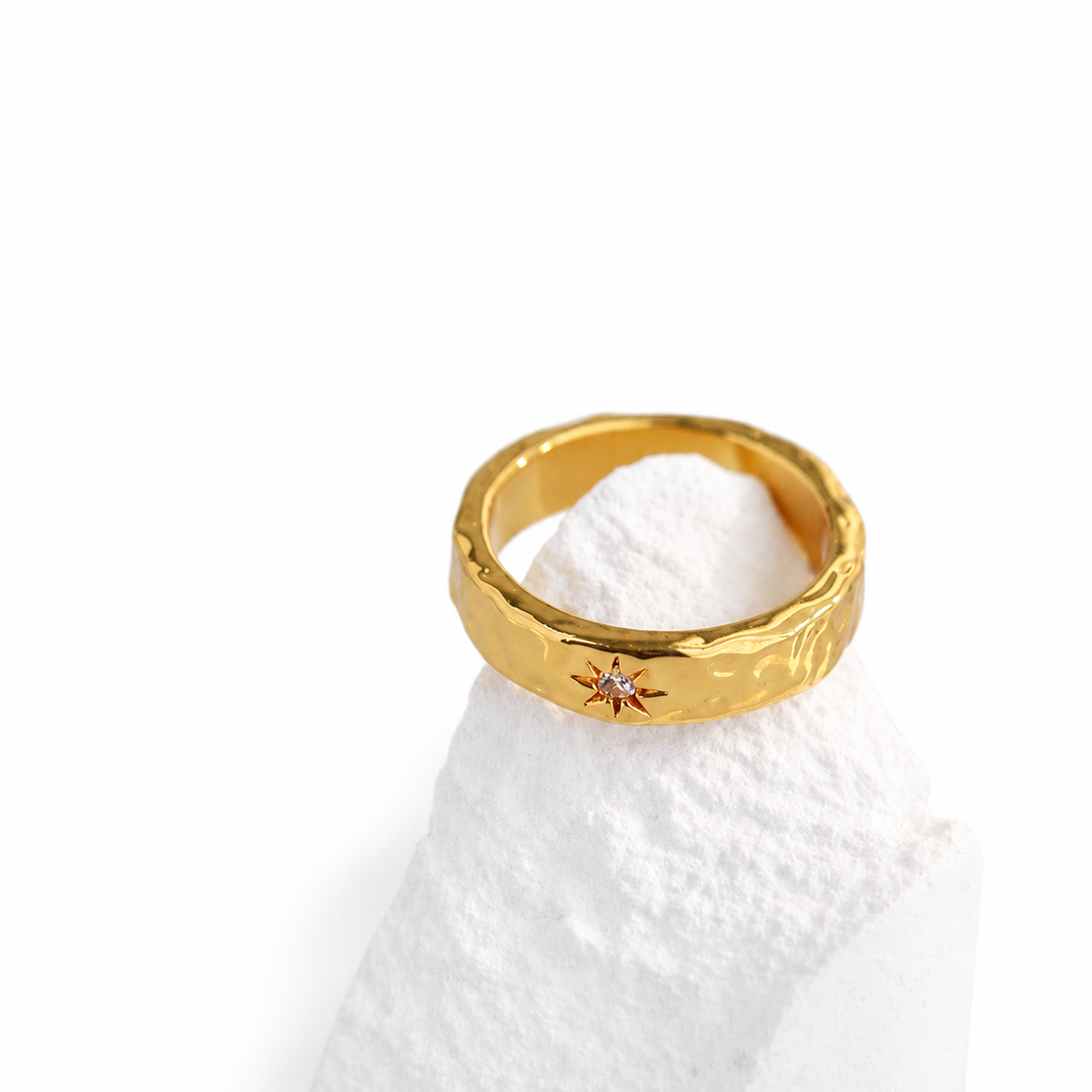 Narrow gold-colored hammered ring with a clear stone in a star-shaped setting.