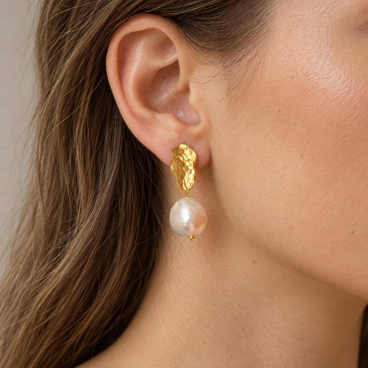 Baroque Pearl Drops Earrings worn on one ear, showing the sculptural gold-tone form and pearl drop.