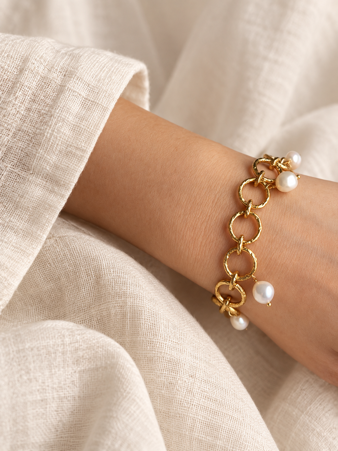 Freshwater pearl charm bracelet with gold-plated circular links shown on a wrist beside an ivory sleeve.
