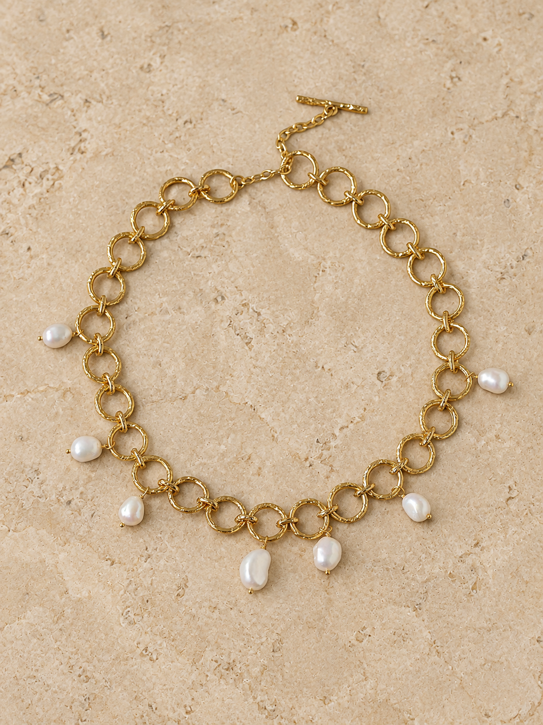 Complete textured-link necklace with seven freshwater pearl drops on pale limestone.