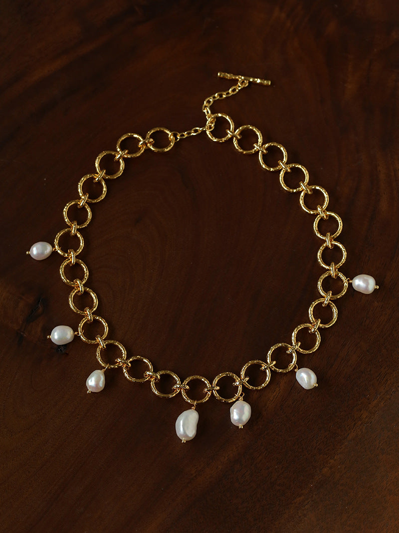 Textured gold-tone circular-link necklace with seven irregular freshwater pearl drops on dark wood.